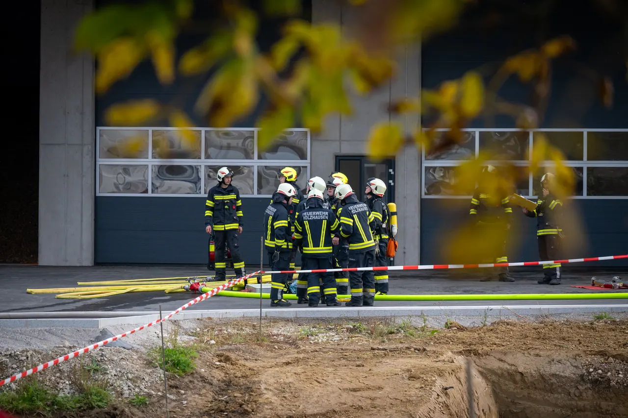 Feuerwehrleute mit Atemschutzausrüstung vor einem Feuerwehrhaus, davor ein abgesperrter Übungsbereich