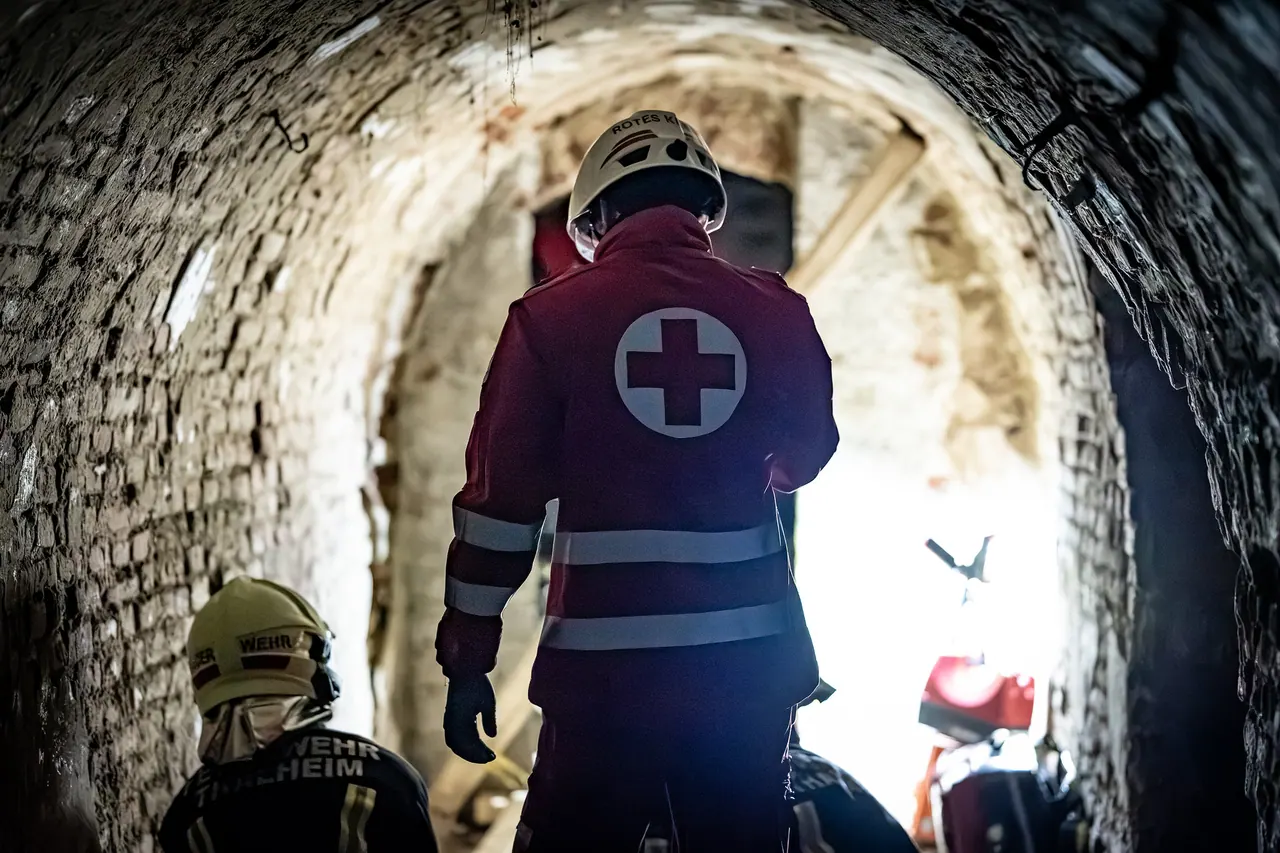 Einsatzkraft des Roten Kreuzes von hinten in einem gemauerten Gewölbegang, im Hintergrund helles Licht